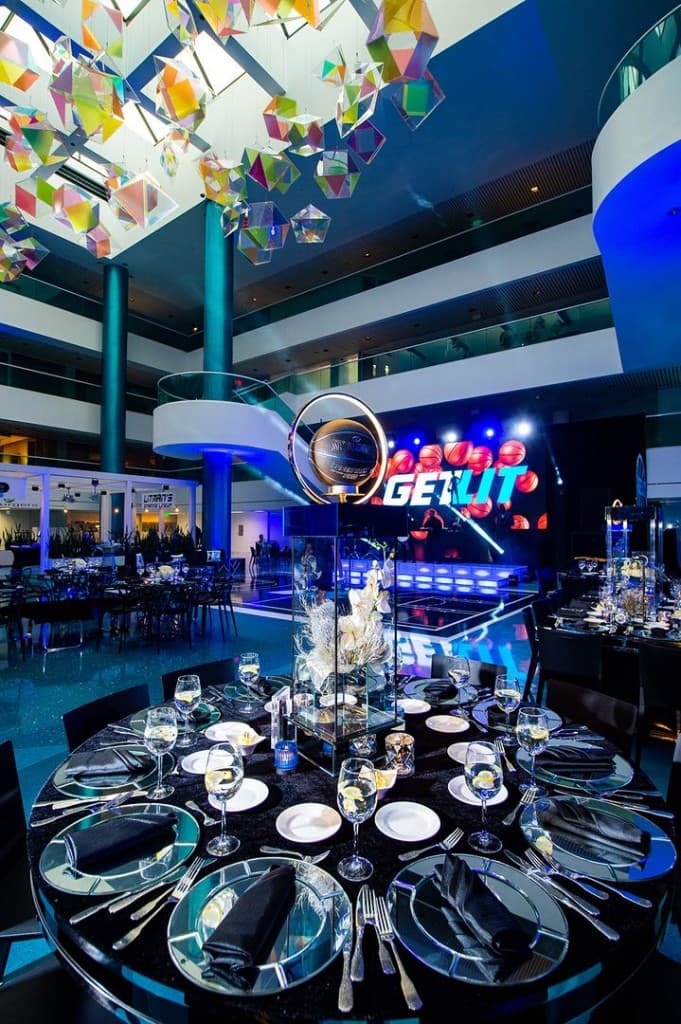 Atrium B gala with round tables, blue lighting, and stage screen for a branded social event