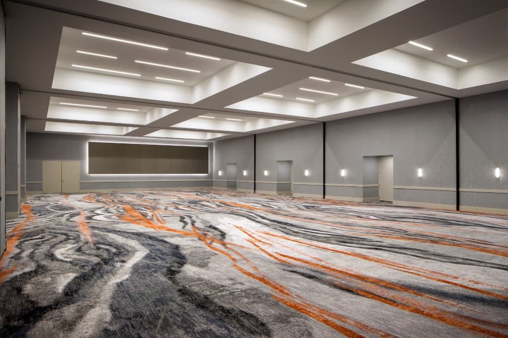Aqua Vista ballroom empty: tiered ceiling with linear lighting, neutral walls, and abstract gray carpet with orange accents