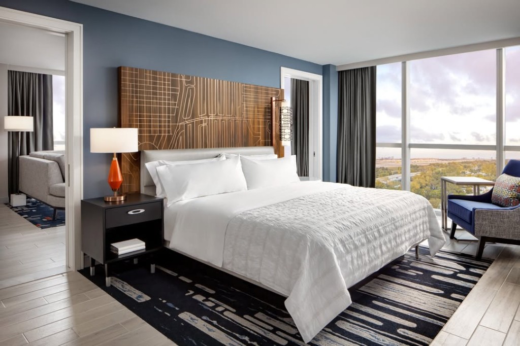 Hotel bedroom suite with king bed, slate accent wall, seating by floor-to-ceiling windows